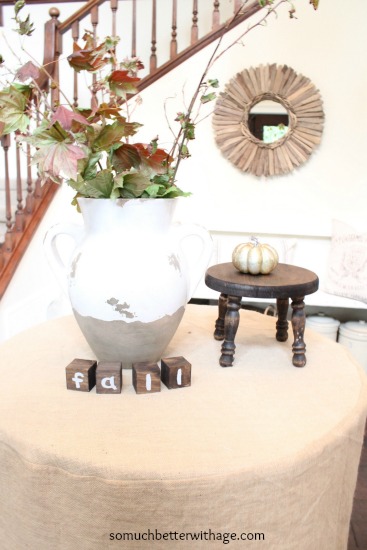 Large white vase filled with branches and leaves in foyer.