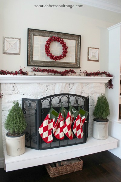 White fireplace mantel with red berries on it and a red wreath above it.