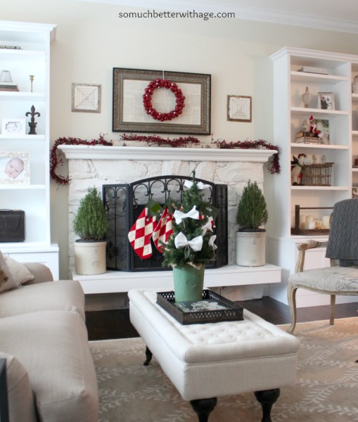 Open shelves, white ottoman with Christmas tree on it and red berries on top of mantel.