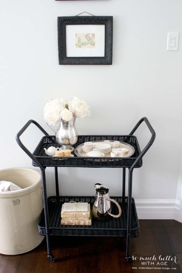 Dark wicker serving cart with a pitcher, cookies, plates and flowers.