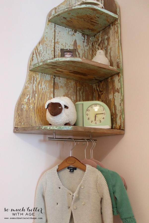 A wooden distressed shelf holding a child's clock, and stuffed animal.