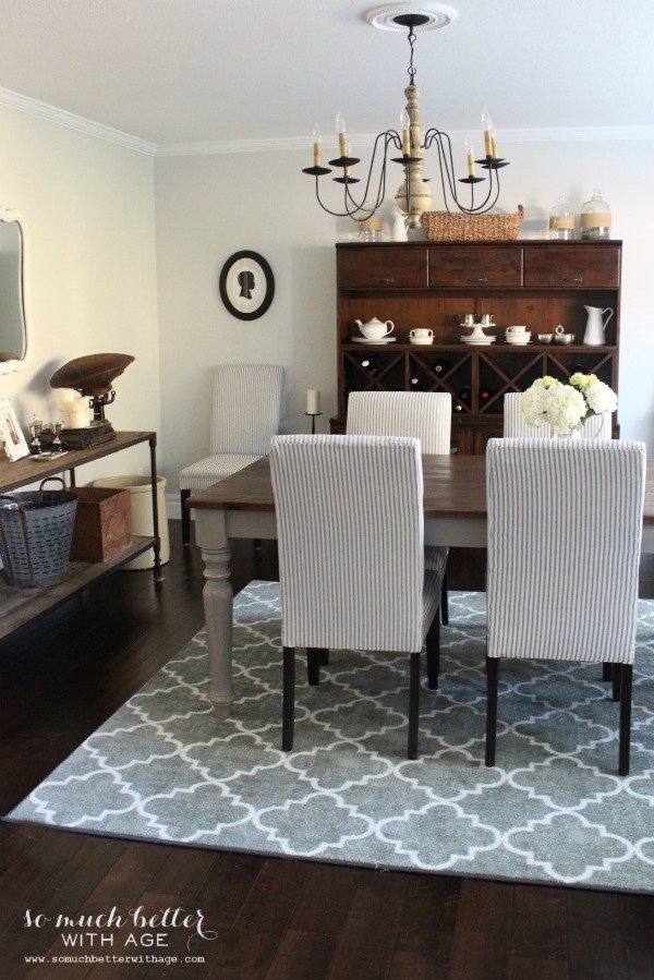 A dining room with a rug underneath in a grey and white.