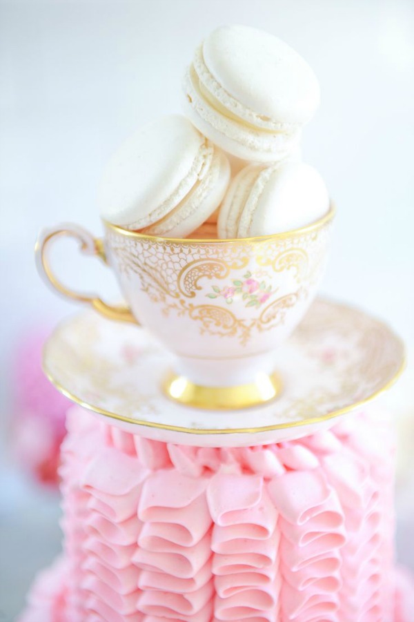 A teacup filled with white macarons on top of a cake.