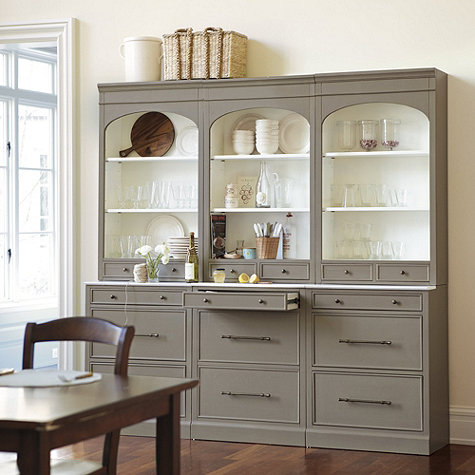 A light grey wooden cabinet with a drawer opened and glasses on the shelves.