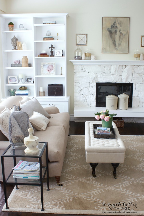 Neutral coloured couch in the living room with the white fireplace and crocks on the mantel.