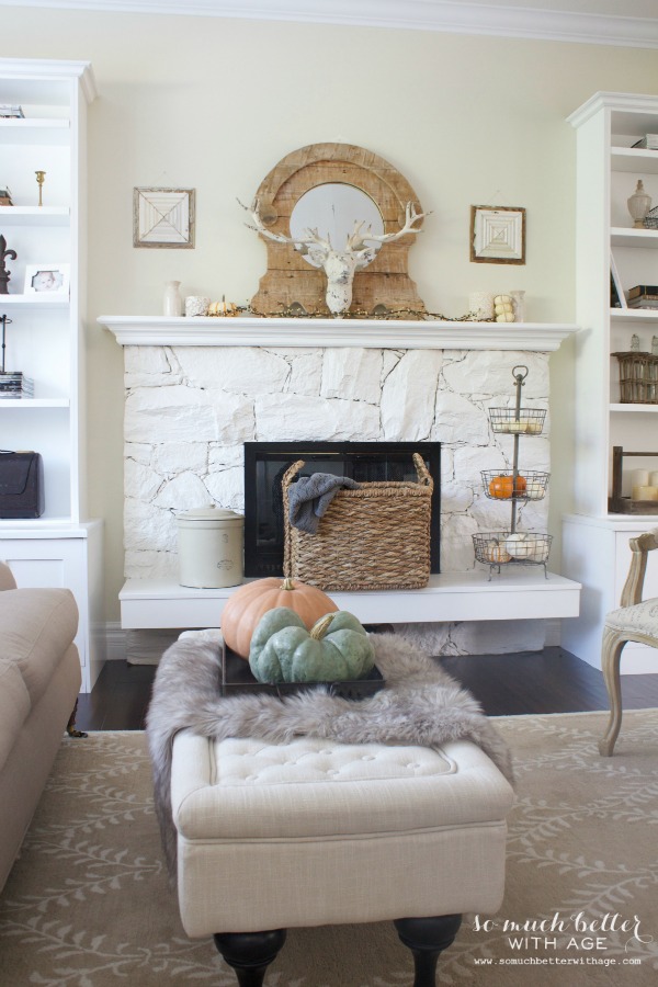 A whitewashed fireplace with a mirror on the mantel and antlers on the mirror.