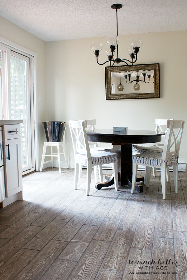 A dining room table that is round, with a light fixture above it, and a antique mirror on the wall.