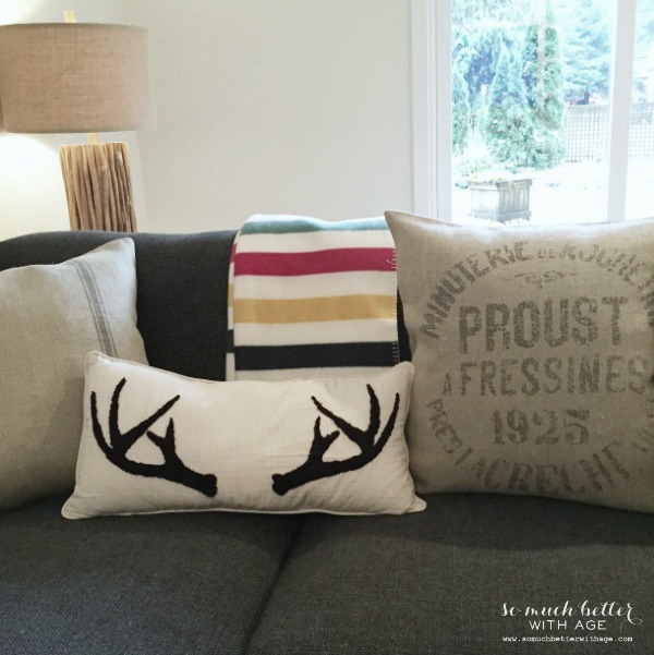 A grey couch with an antler pillow and striped throw blanket.