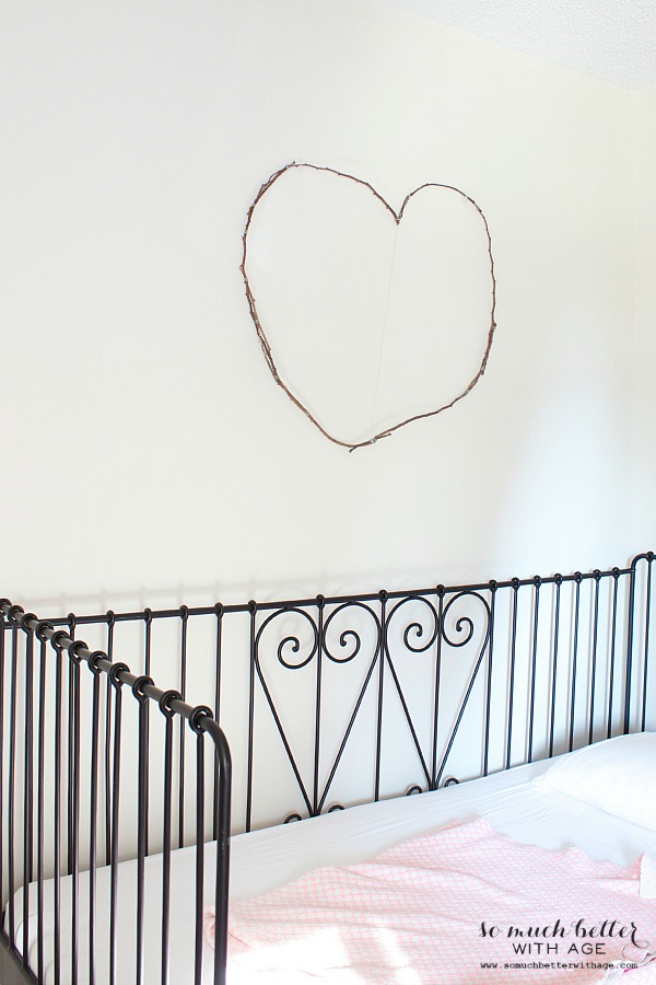 A twig heart hanging on the wall above the bed.