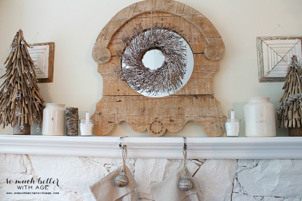 The fireplace mantel decorated with a wooden mirror and wreath hanging on it, plus neutral Christmas stockings are hanging above the fireplace.