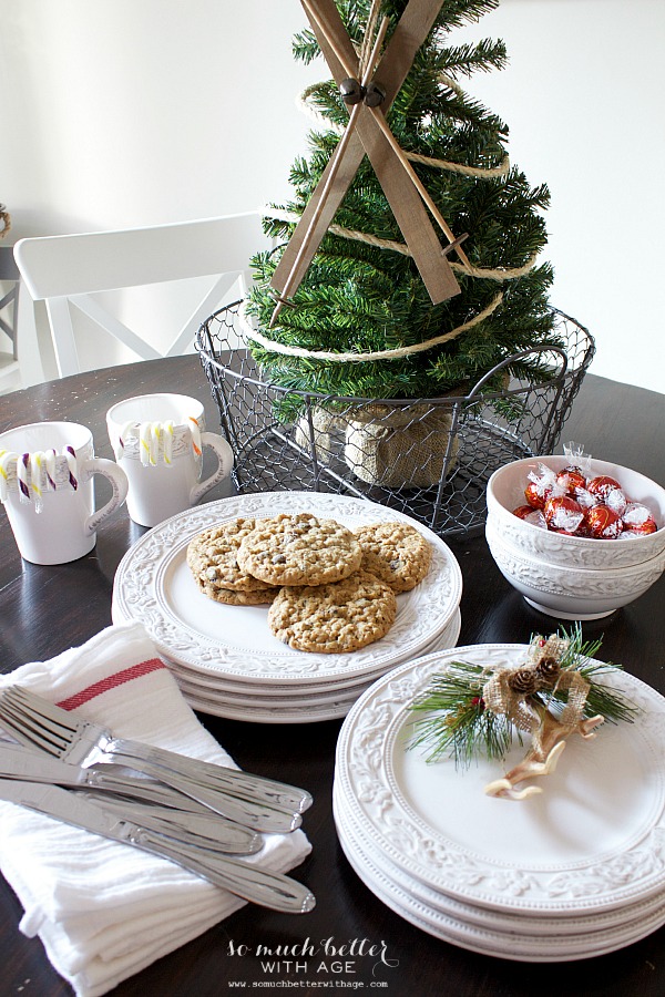 White plates stacked on the table with cookies on it and a mini Christmas tree on the table too.