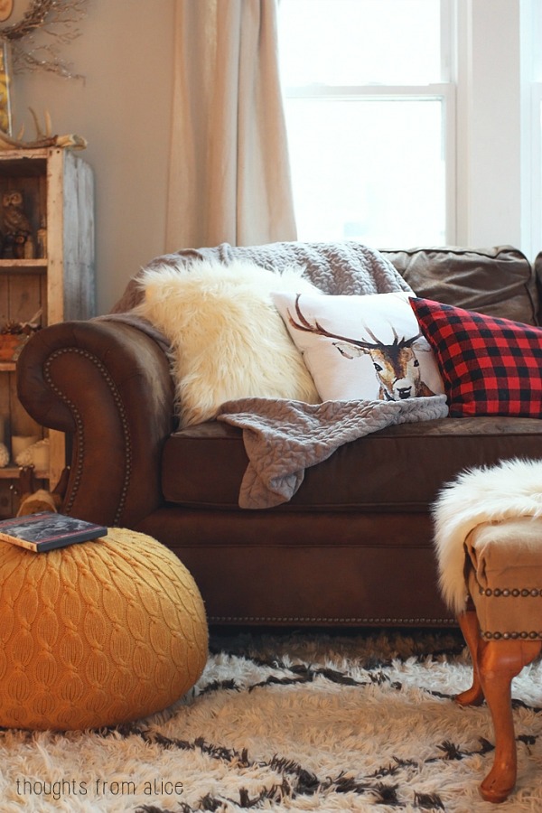 A dark brown couch with a white faux fur pillow and a deer pillow on it.