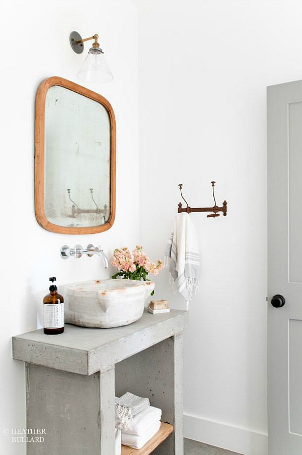 A concrete bathroom sink with a wooden mirror.
