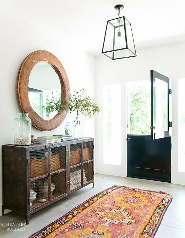 A rustic entryway and a wooden round mirror and a rug in the hallway.