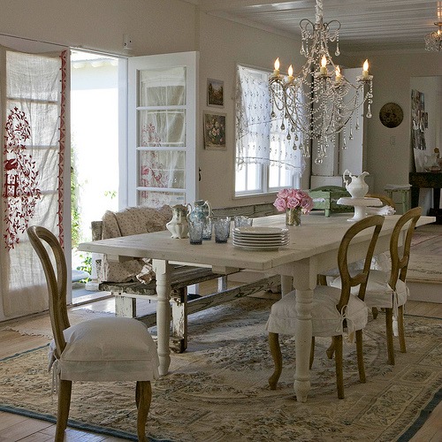 A large chandelier over top of the dining room table with a door open to the veranda.