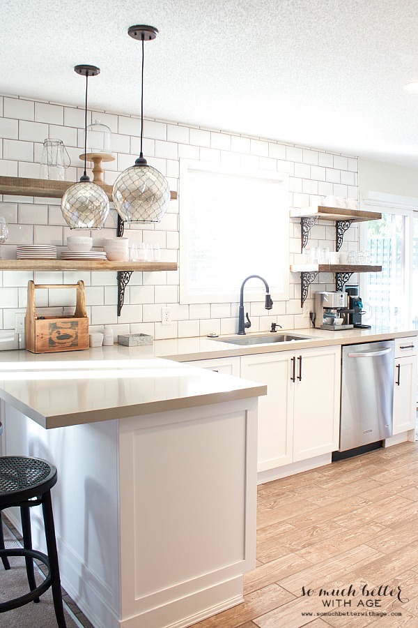 A mostly white kitchen with subway tile and open shelves.