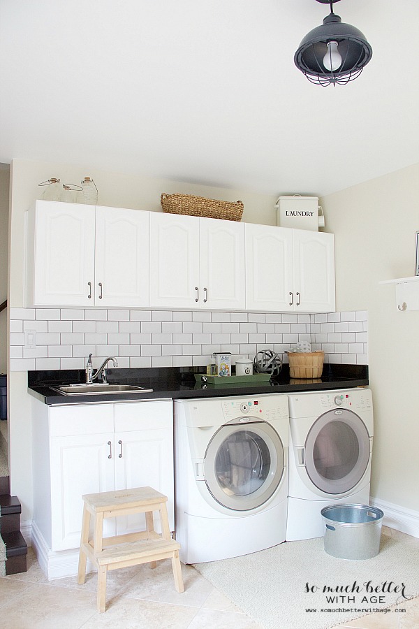 The same laundry room with white cabinets, subway tile, and a black countertop.