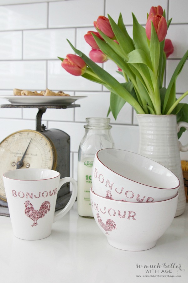 Teacups that say bonjour on them beside a vintage scale.