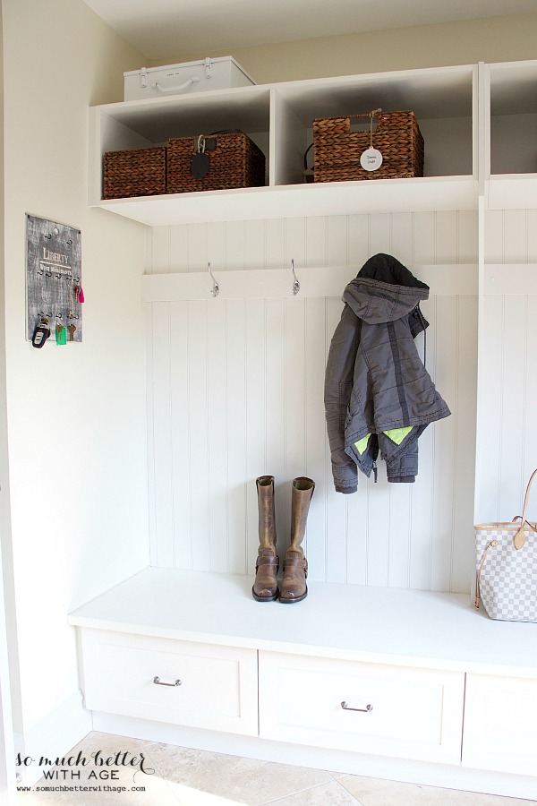 Laundry room built-in cubbies with a jacket hanging on the hooks and boots underneath it.