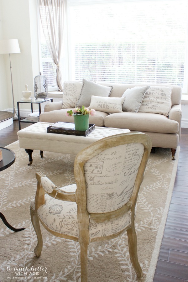 There is a neutral couch with French inspired cushions and a wooden and Parisian armchair.