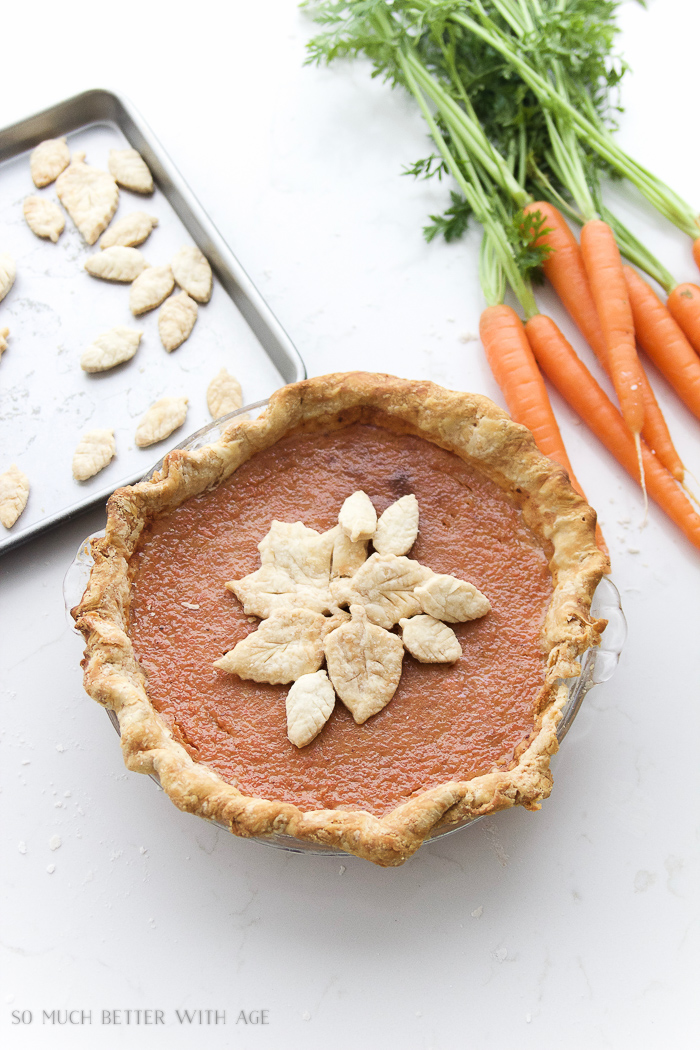 Orange carrot pie with carrots lying on counter.