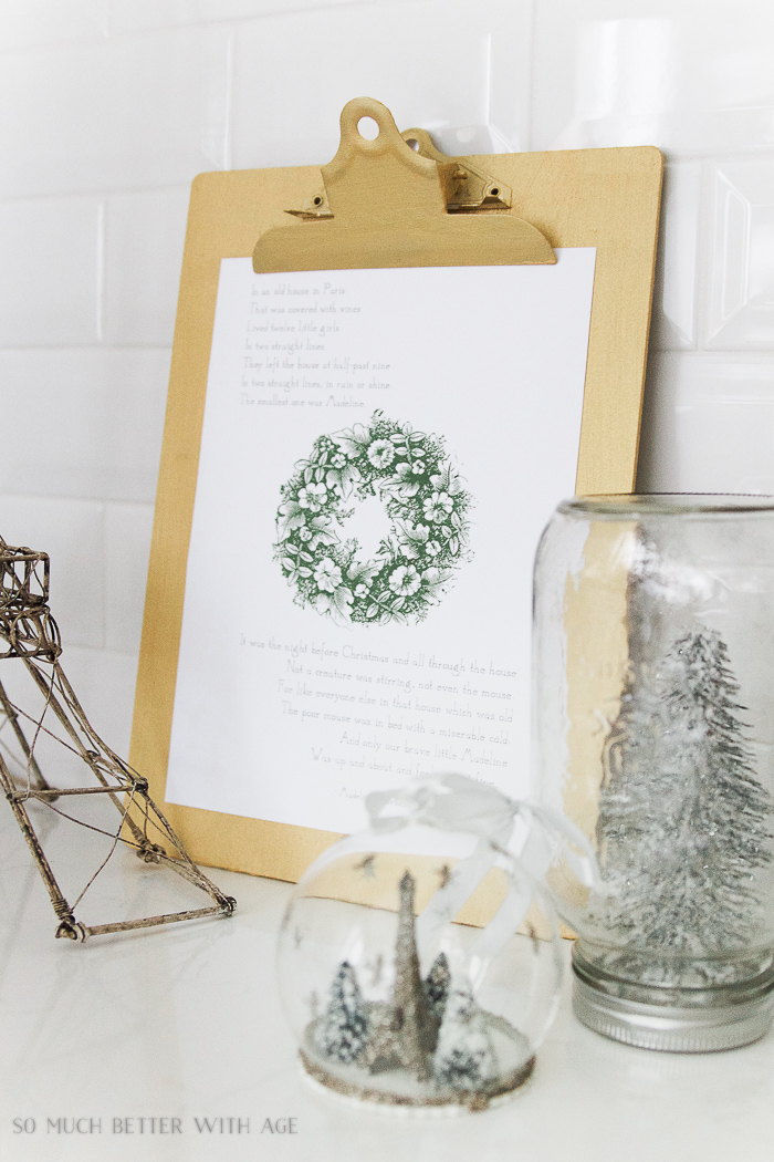 The printable on a clipboard beside mini Christmas trees in a cloche.