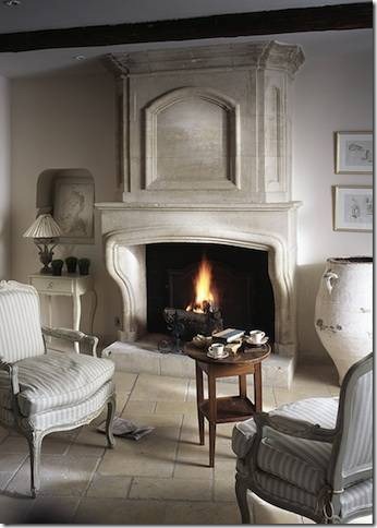 A limestone fireplace with a small fire going in it.