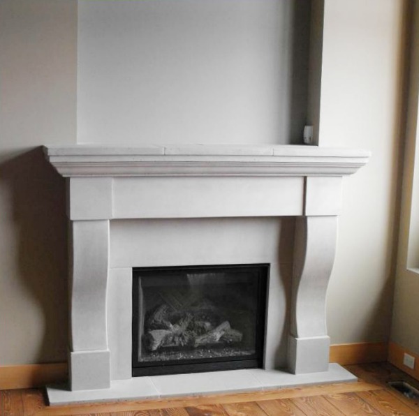 A white stone fireplace wth a wooden floor.