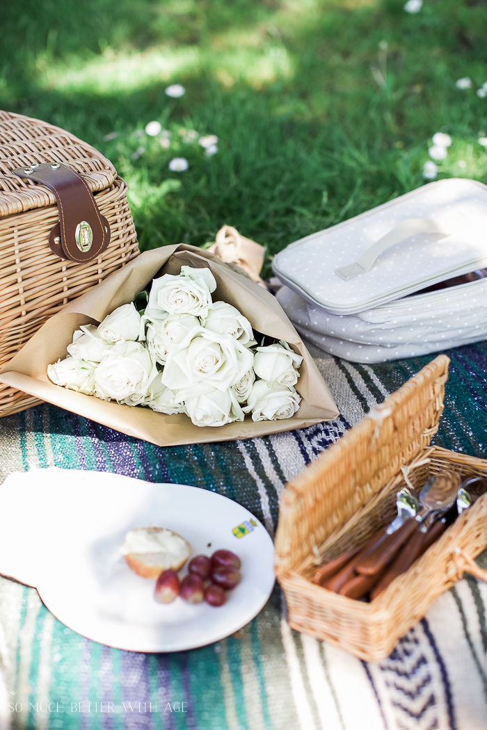 A bunch of white roses are on the picnic blanket.