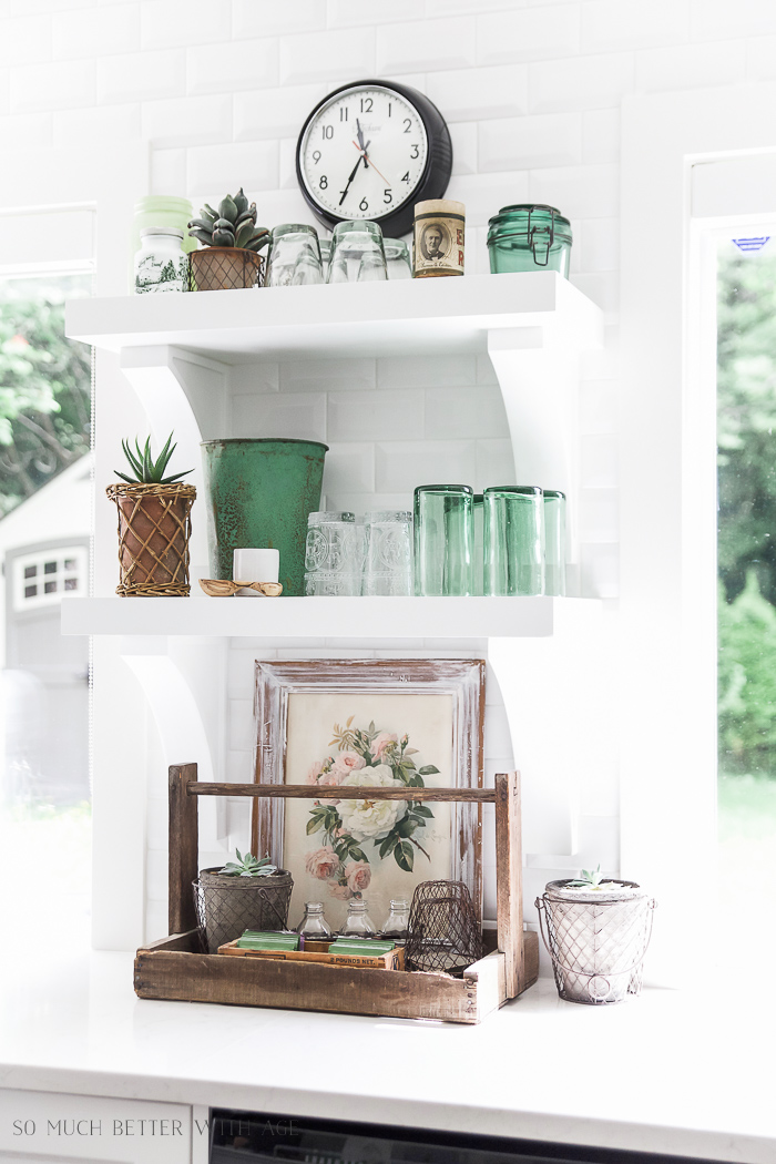 Green glasses sit on a white shelf in the kitchen.