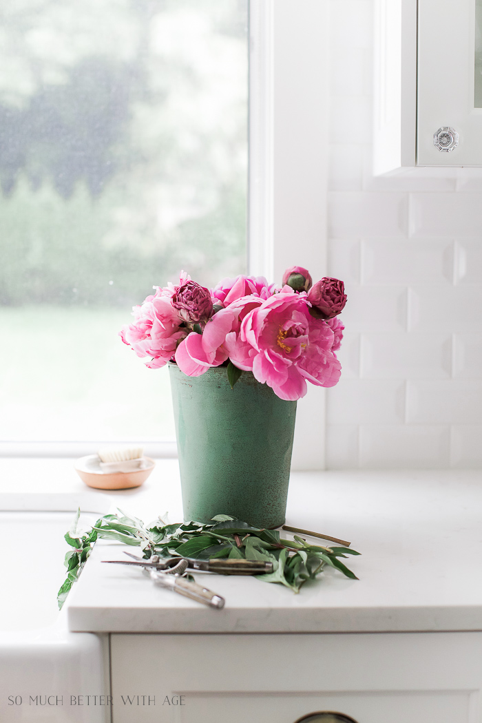 Pink peonies in a green sap bucket on the kitchen counter.