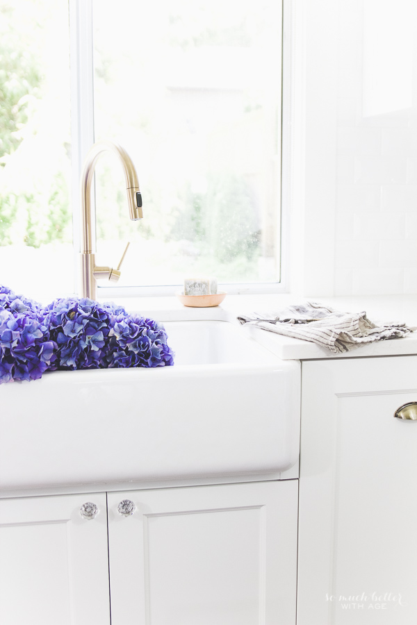 The white sink, with brass faucet and purple hydrangeas in the sink.