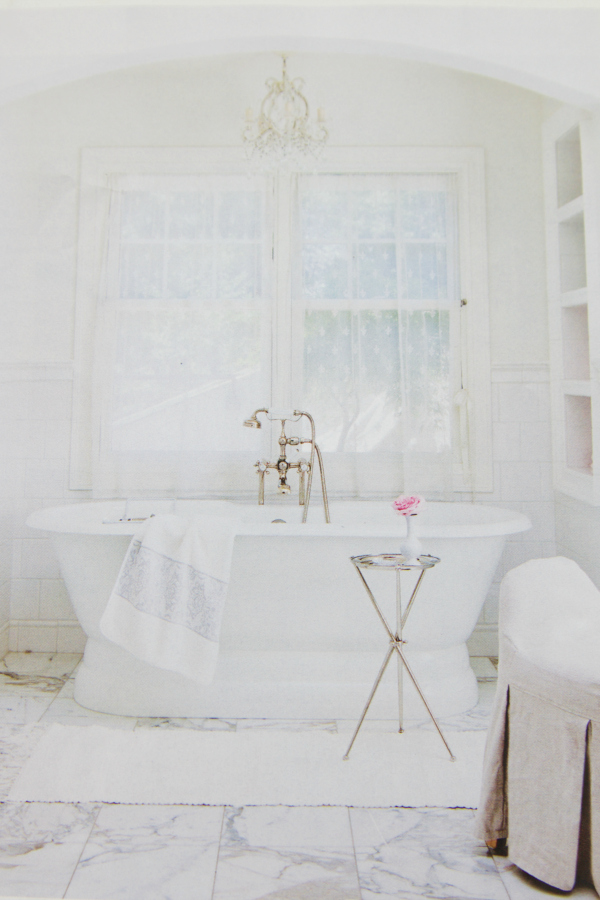 Magazine page opened to white bathroom with chandelier and old fashioned tub.