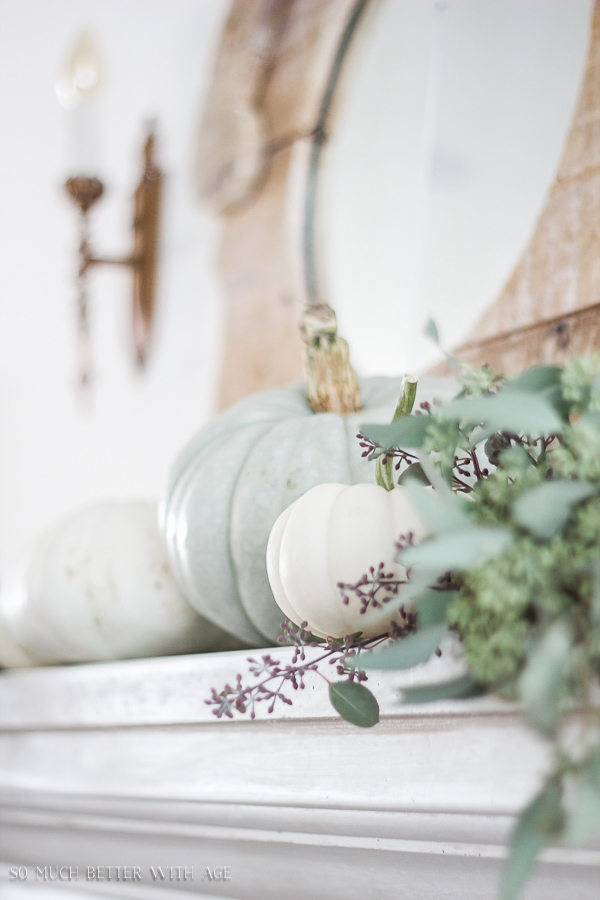 There are pumpkins on the mantel beside the eucalyptus.