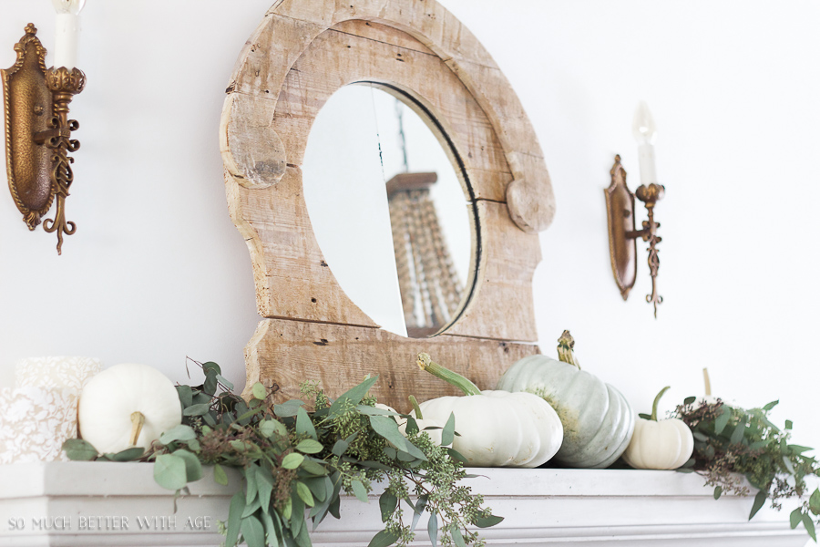 There is a large wooden mirror on the fireplace mantel with wall sconces beside it.