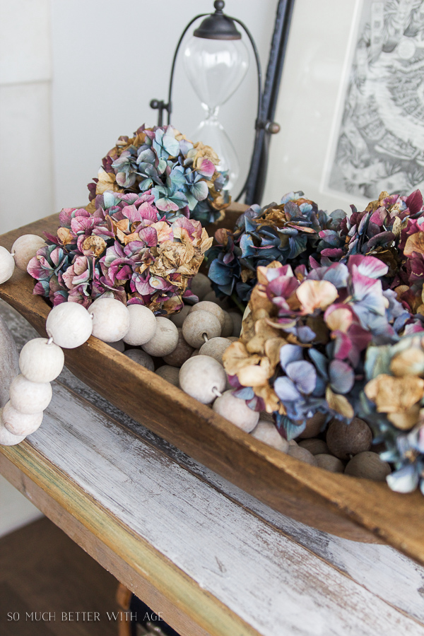 There are wooden beads in the dough bowl beside the hydrangeas.