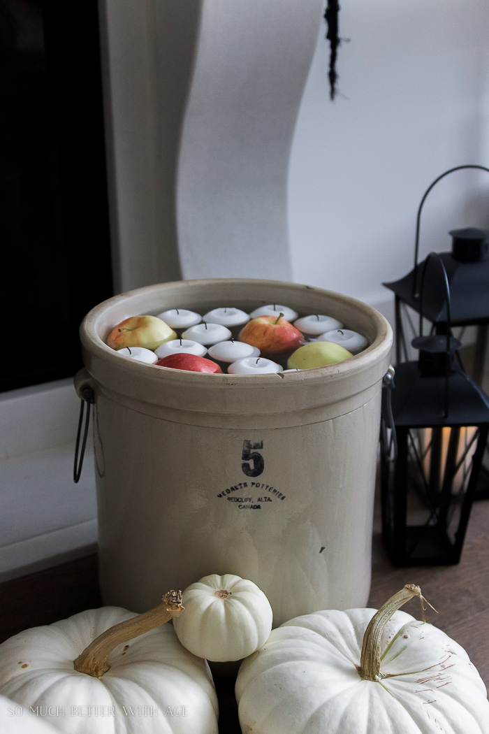 Crock beside the fireplace on the floor and stacked white pumpkins beside it.