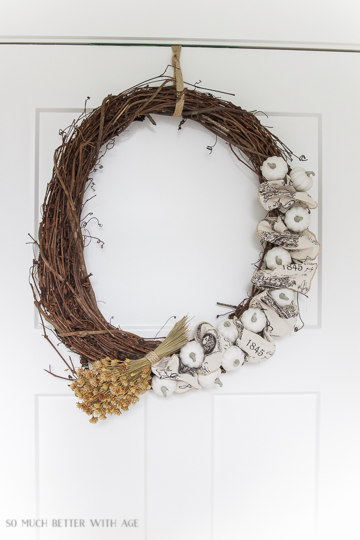 Grapevine wreath with white pumpkins and dried flowers hanging on door.