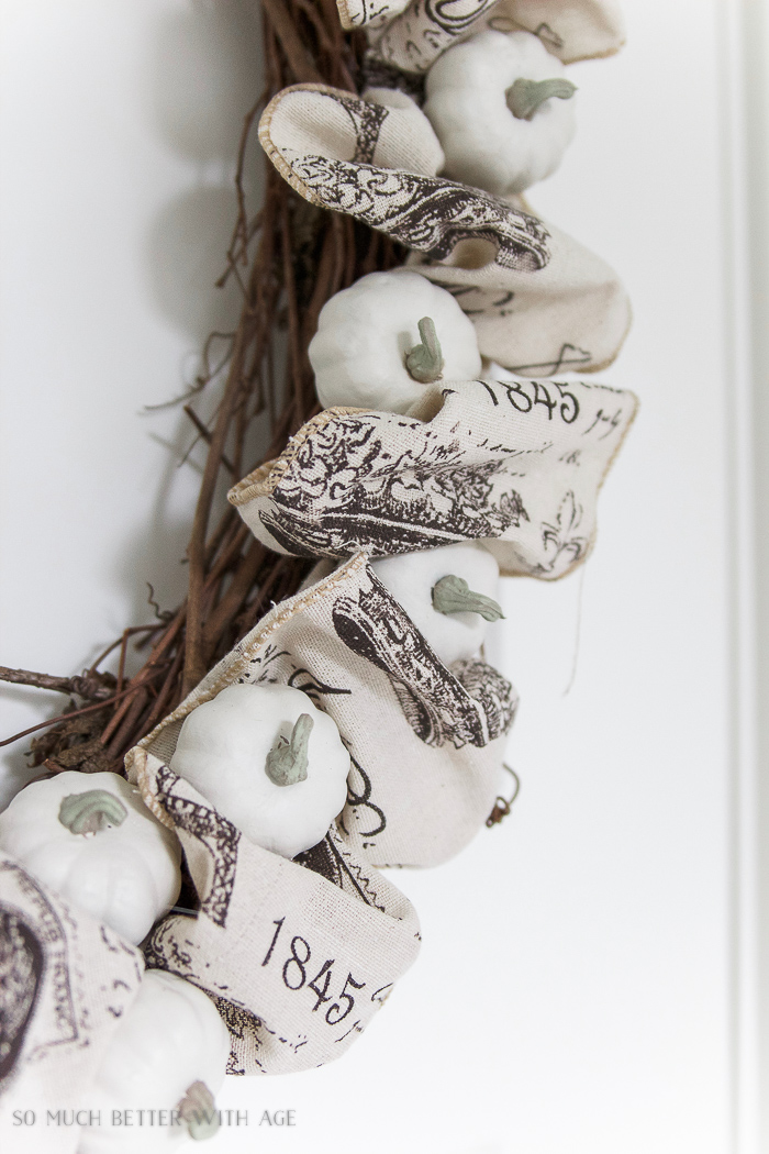 White small pumpkins on wreath with ribbon in between.