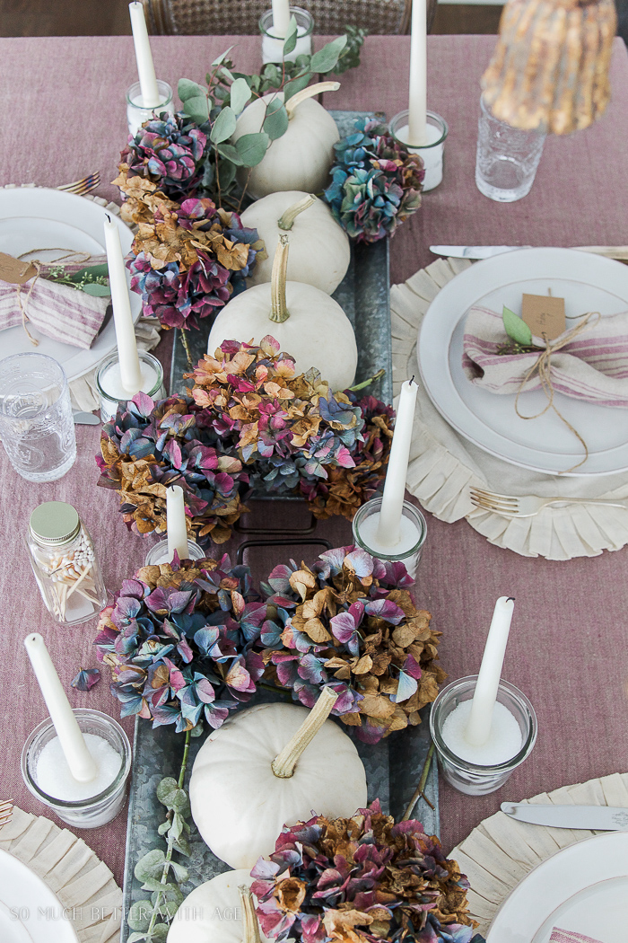 Hydrangeas, white pumpkins on the table with a pink tablecloth.