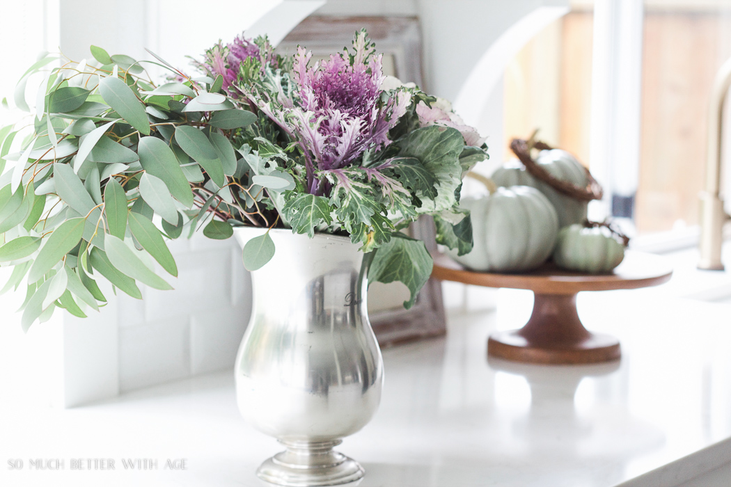 Kale flowers with eucalyptus in silver pitcher.