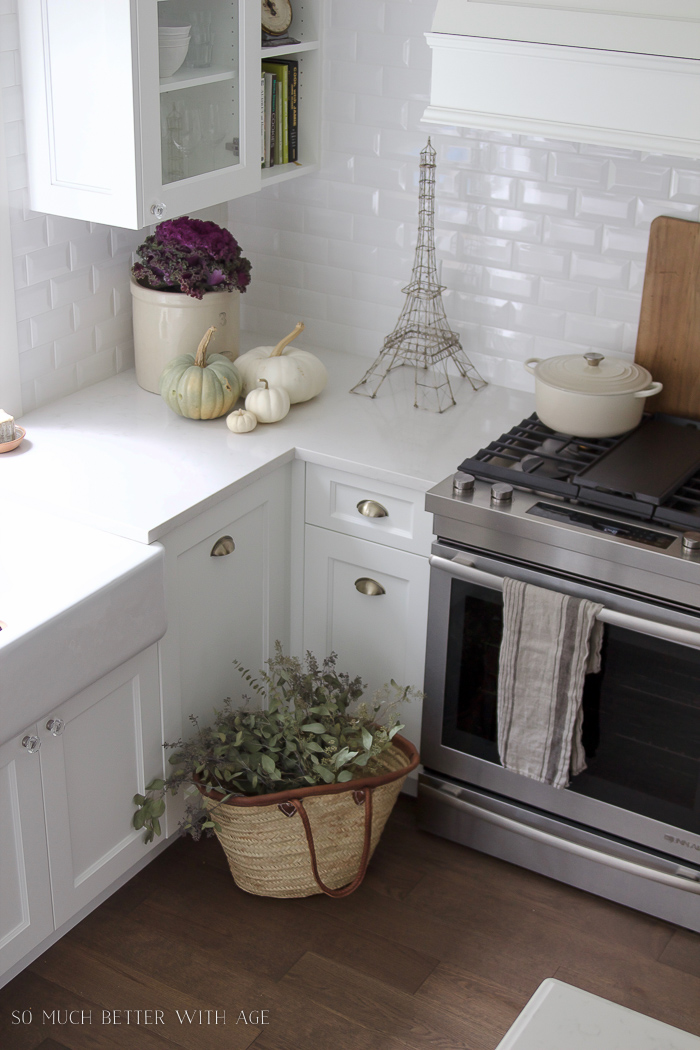 Crock, kale plant, pumpkins, french market basket in white kitchen.