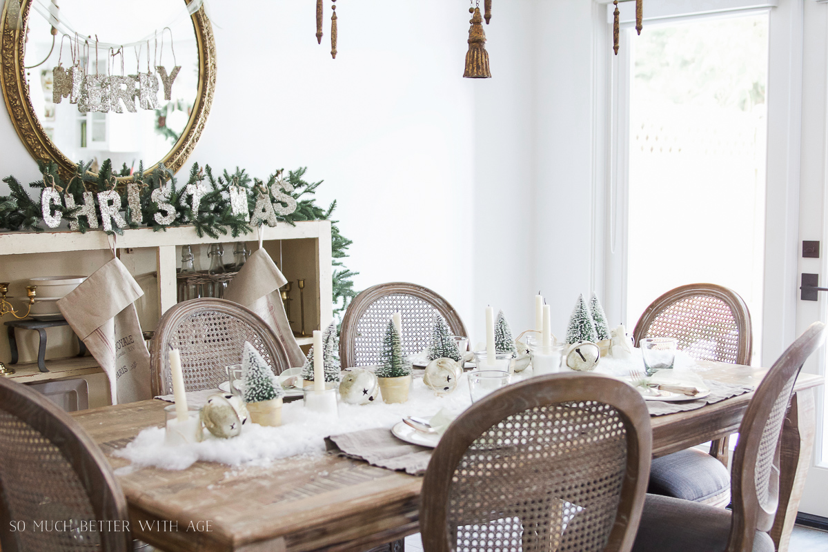 A wooden dining room table with chairs and candles with Christmas decorations on it.