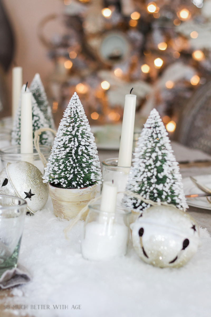 Up close picture of the snowy little Christmas trees beside candles on the table.