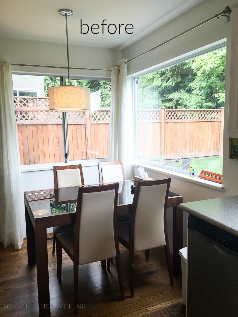 Wooden table with glass top and 4 chairs in corner of kitchen with pendant light hanging down.
