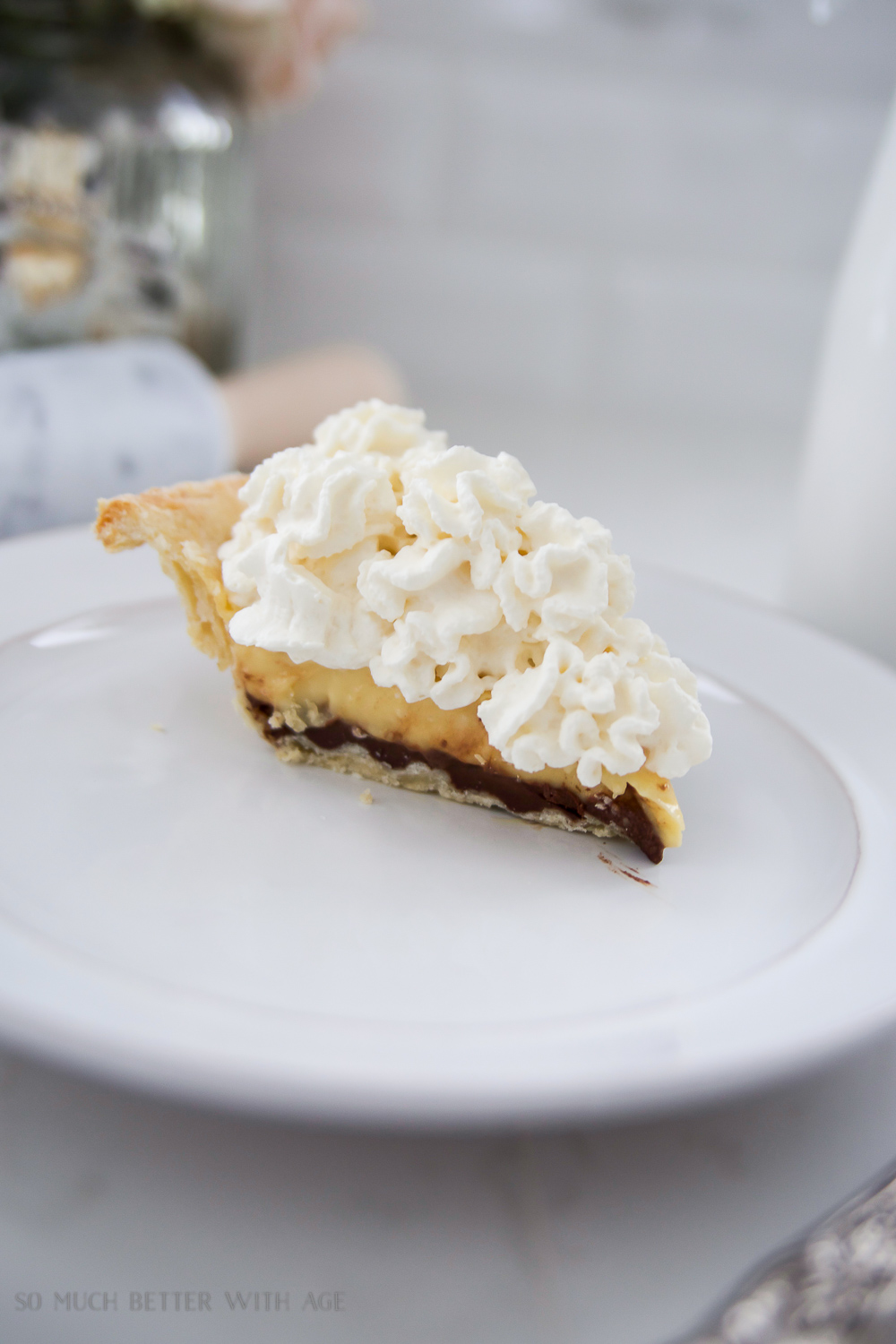 A slice of pie on a white plate with whipping cream on top.