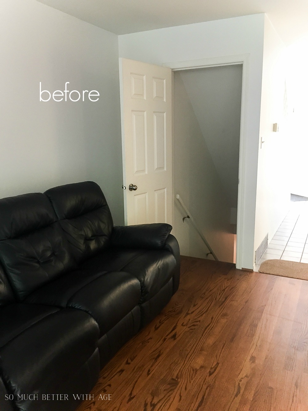 There is a black leather couch beside an open door leading to the basement.