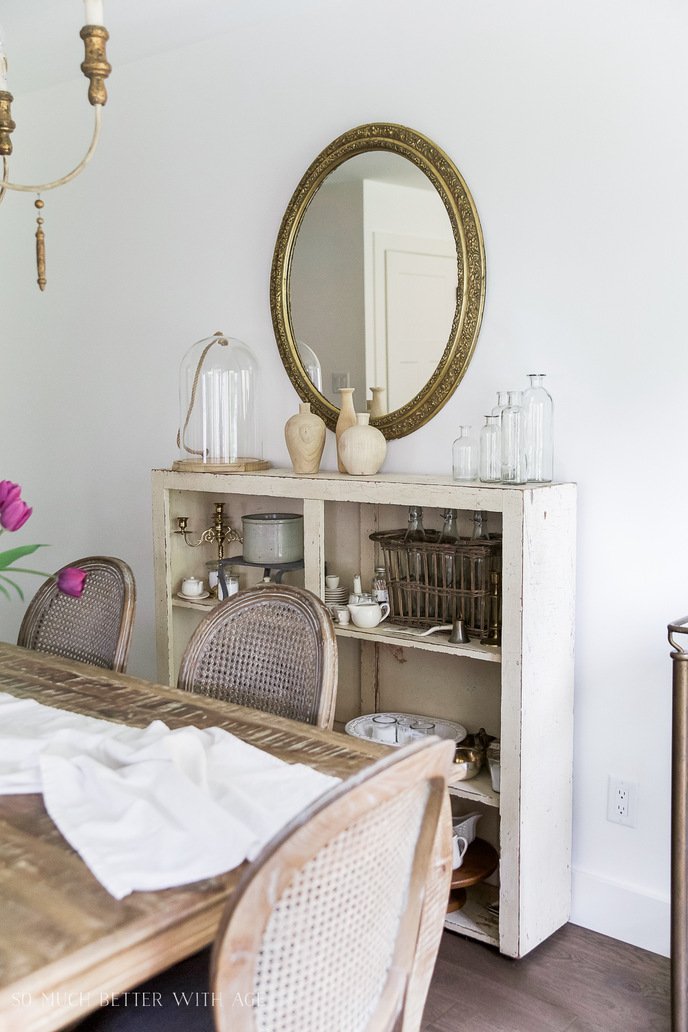 A distressed wooden shelf is behind the table and a round gold mirror is above the shelf.