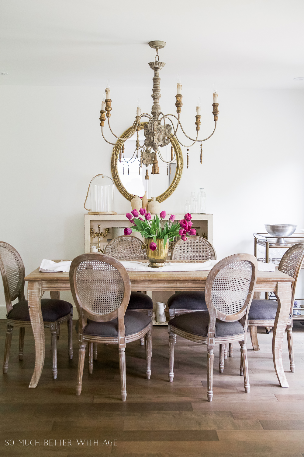 The French vintage dining room with a table, chairs, tulips on the table and a French chandelier above the table.