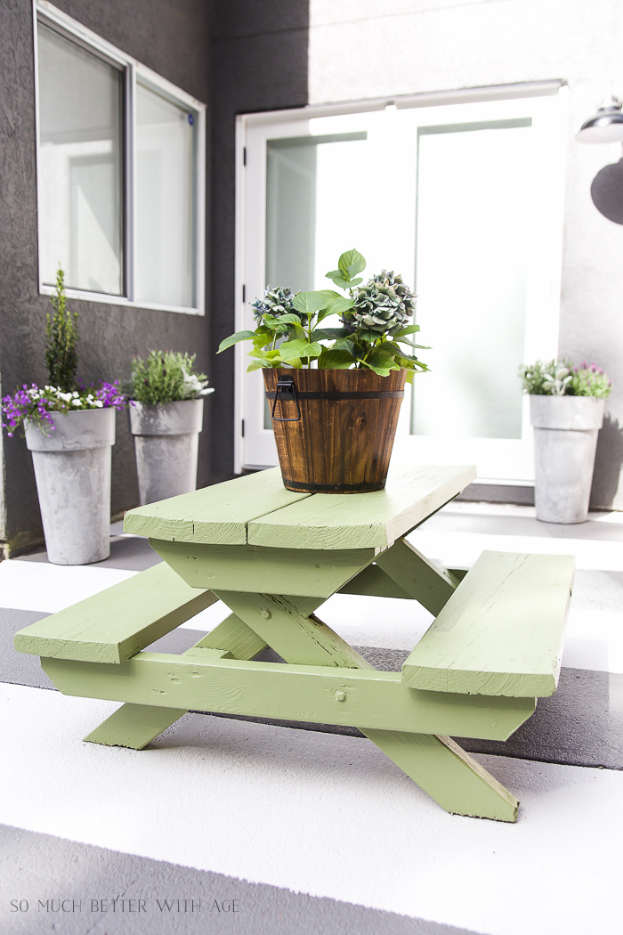 A little green picnic table with a a bucket of flowers on top.